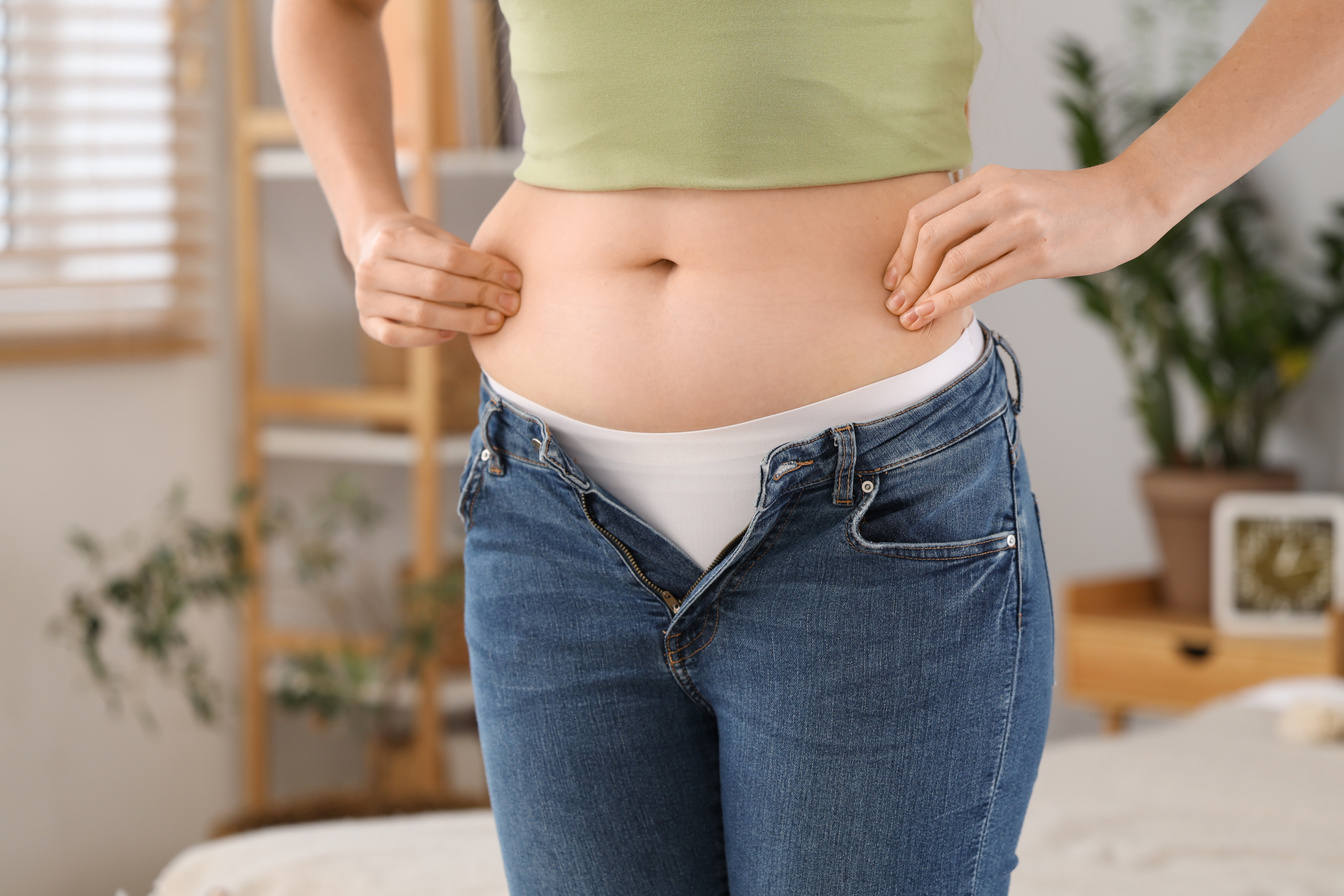 Young Woman in Tight Jeans at Home, Closeup. Weight Gain Concept